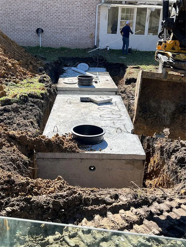 A concrete septic tank is installed in a deep trench in a yard, with heavy machinery visible nearby. septic tank installation in Greenville, NC