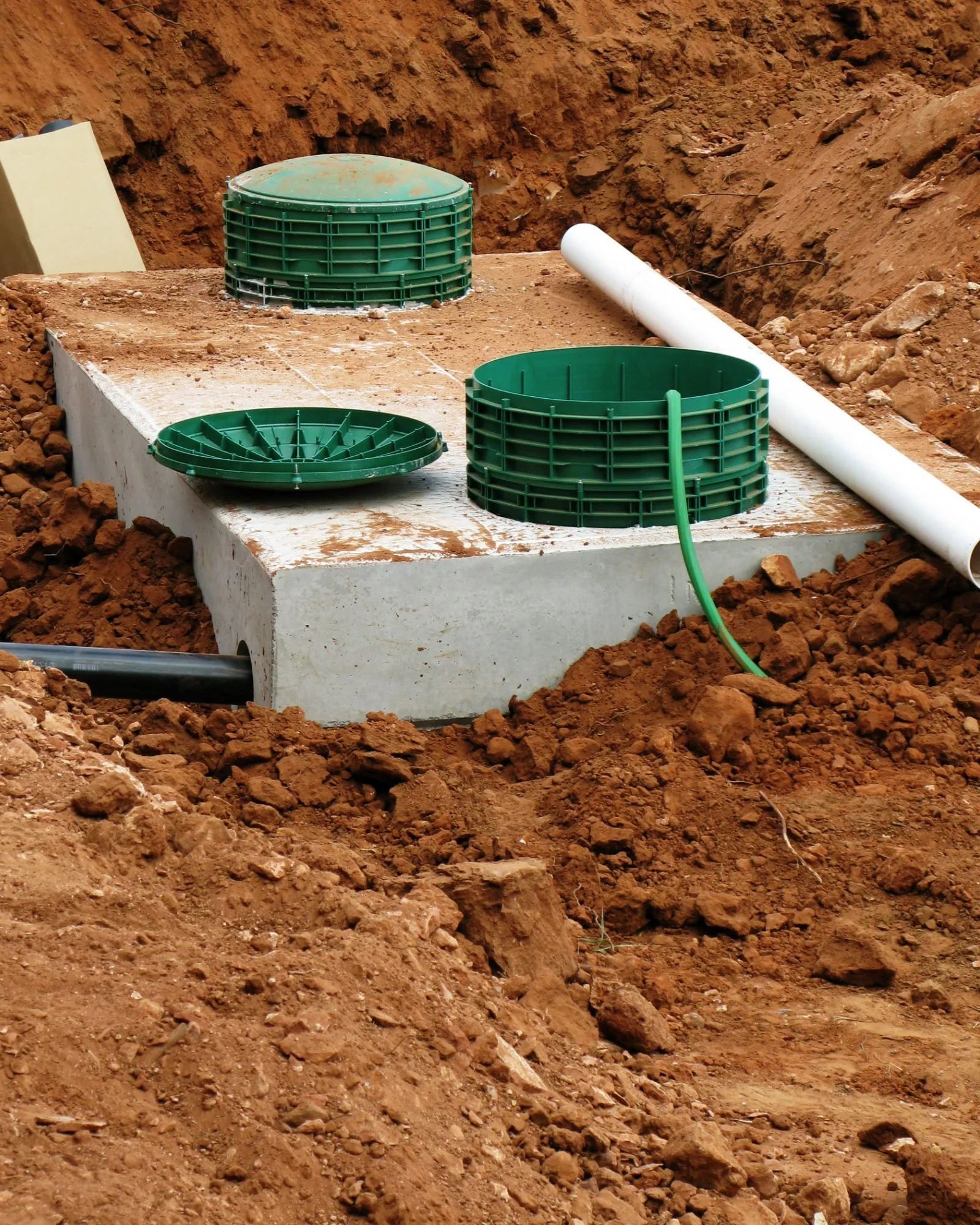Concrete septic tank with green covers and pipes in a dirt excavation. Concrete septic tank with green covers and pipes in a dirt excavation.