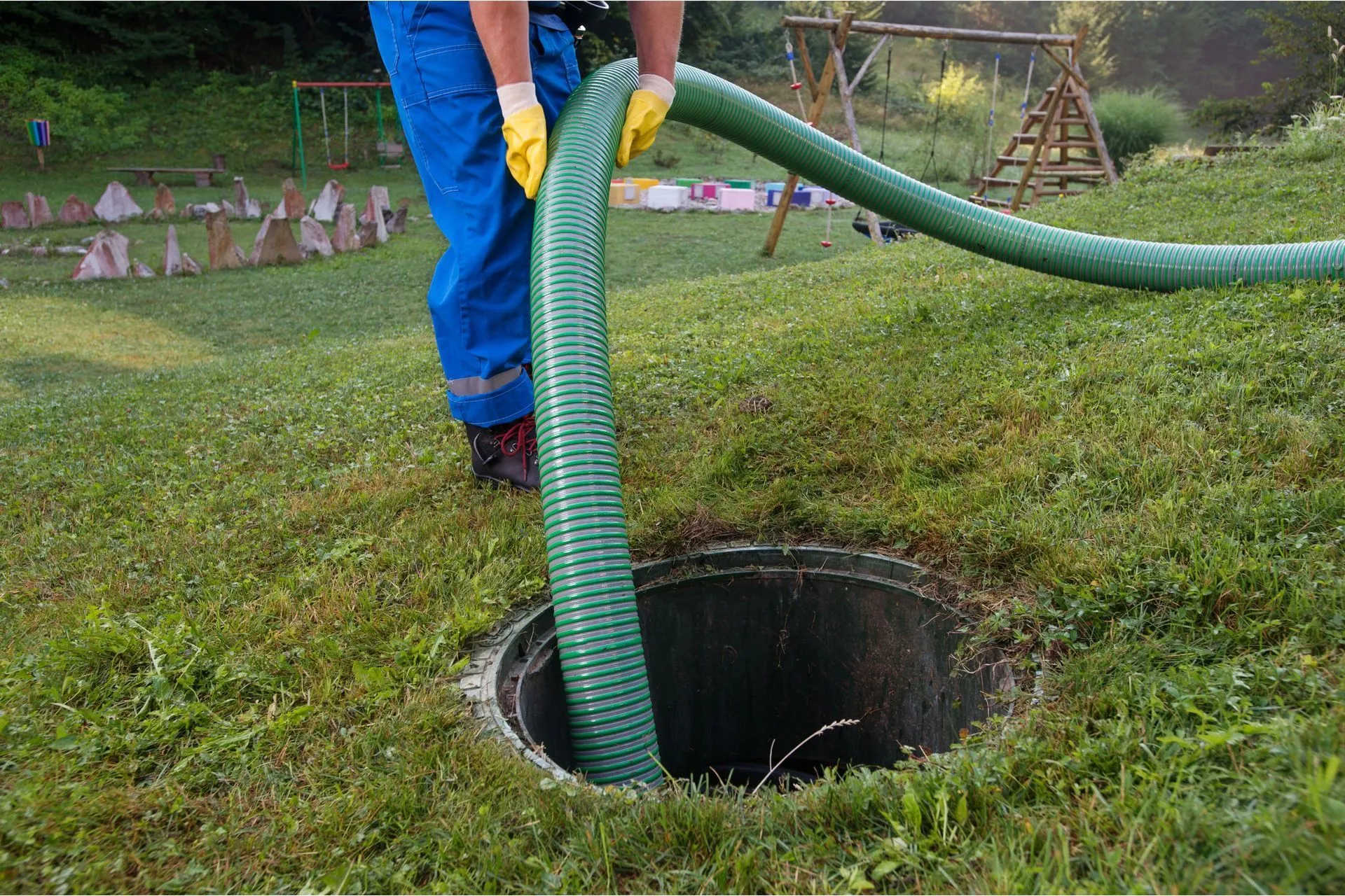 Person in blue jumpsuit and gloves with green hose entering a septic tank. Person in blue jumpsuit and gloves with green hose entering a septic tank.