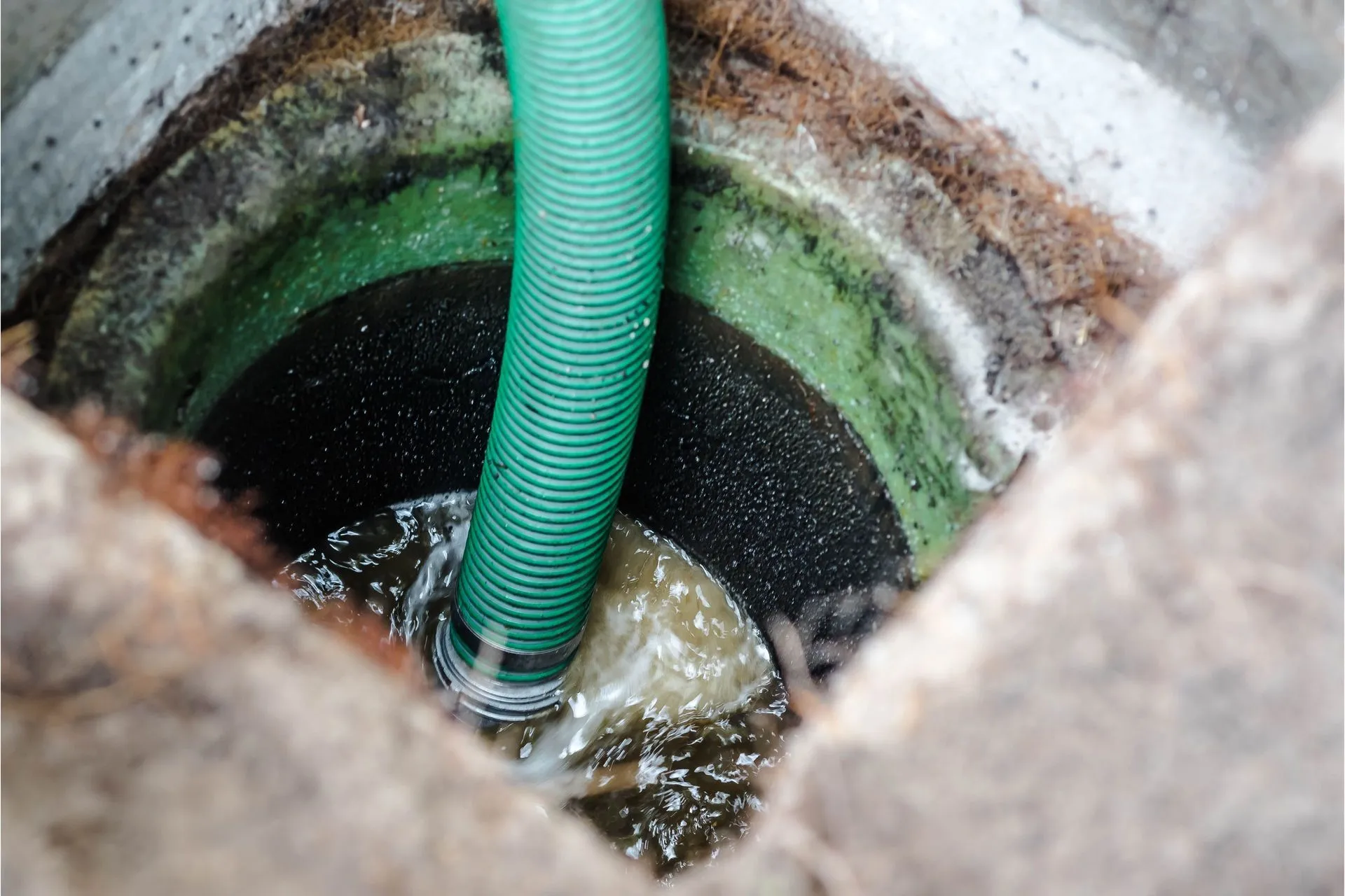 Green hose pumping water from a concrete well. Green hose pumping water from a concrete well.