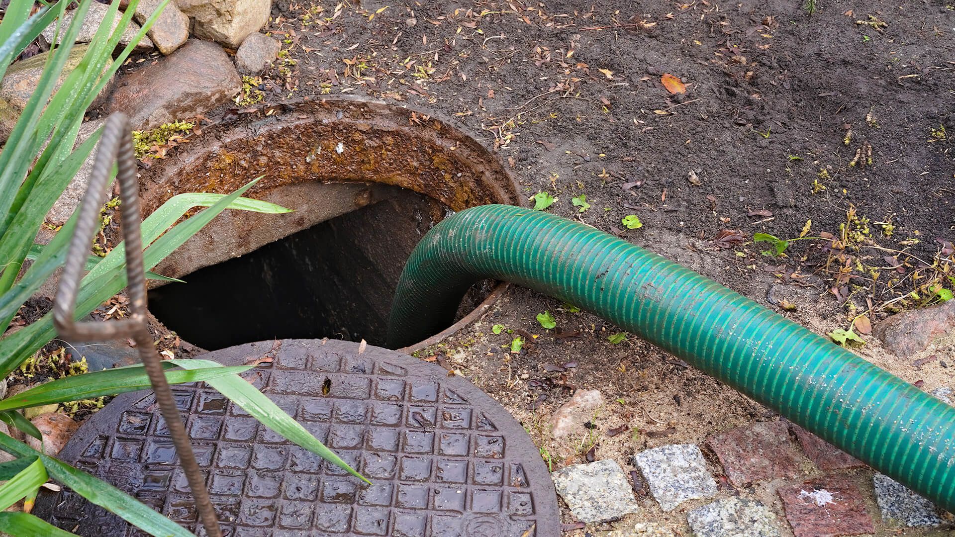 A worker in a red hard hat uses a yellow suction hose to clean out a dark, circular utility manhole. septic tank repair in Greenville, NC